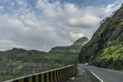 Empty road by mountains against sky