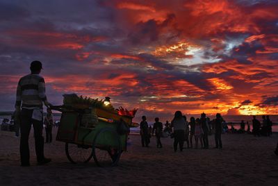 Full length rear view of vendor selling sweetcorns at beach against orange sky