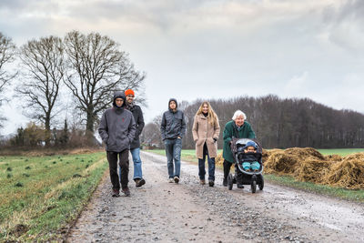 Family walking on dirt road against sky