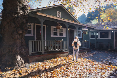 A woman with a child is standing near a house on yellow leaves