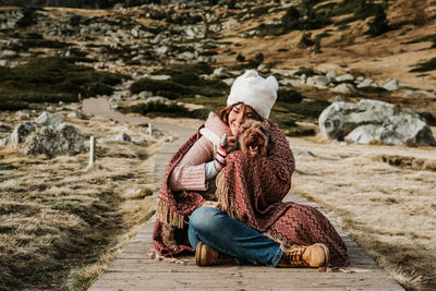 Woman wearing knit hat sitting in footpath with dog against field