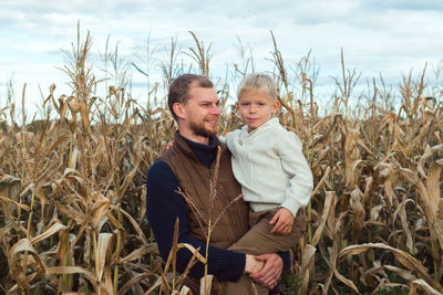 Family walking in corn field at autumn, dad and son posing among high plants