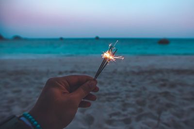 Cropped hand holding sparkler at beach