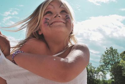 Low angle view of happy girl with face paint against sky