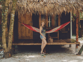 Full length of beautiful woman standing against hut