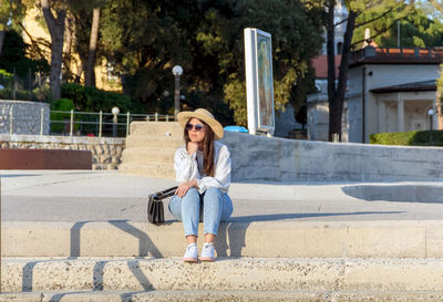 Front view of young woman sitting alone on concrete stairs in city.