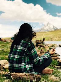 Rear view of woman sitting on field against sky