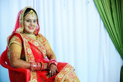 Close-up of bride sitting on chair against curtains