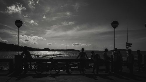 People sitting on street by sea against sky