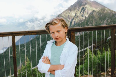 Portrait of smiling boy standing by railing against mountain