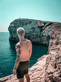 Man standing on rock by sea against clear sky