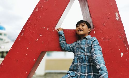 Low angle view of smiling woman standing against red wall