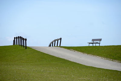 Empty park bench on field against sky