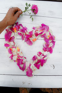 Cropped hand of man holding rose over heart shape petals at table