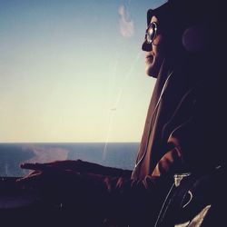 Close-up of young woman sitting by sea against sky
