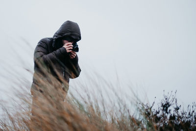 Man photographing while standing at field against sky