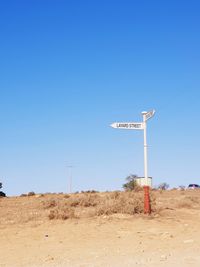 Road sign on desert against clear blue sky