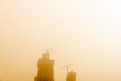 Cranes at construction site against sky during sunset