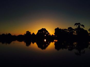 Reflection of silhouette trees in water at sunset