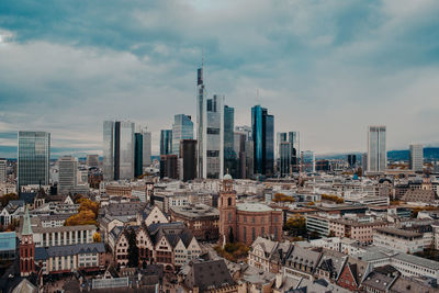 Aerial view of buildings in city against cloudy sky