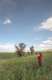 Young woman happy with raised arms in the field with red poppy anemone flowers in spring. 