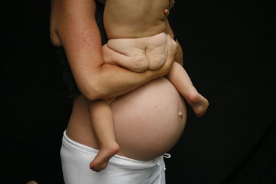 Midsection of pregnant mother with naked baby against black background