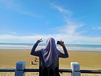 Rear view of woman standing at beach against sky