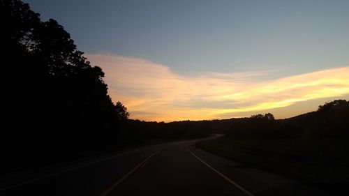 Road amidst silhouette trees against sky during sunset