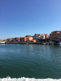 Sea by townscape against clear blue sky