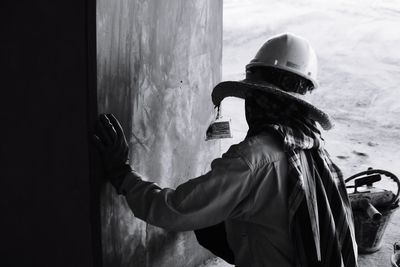 Rear view of man working while standing by wall