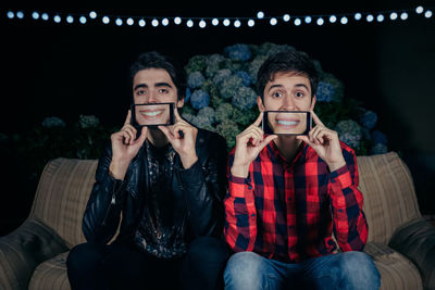 Portrait of young friends holding smart phones on face while on sofa during party