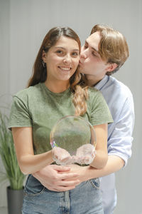 Man kissing woman while standing against wall at home