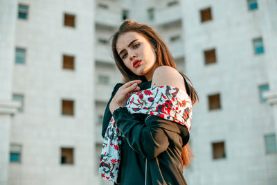 Portrait of beautiful woman standing against buildings in city