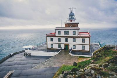 Lighthouse amidst buildings by sea against sky