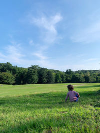 Rear view of woman sitting on field against sky