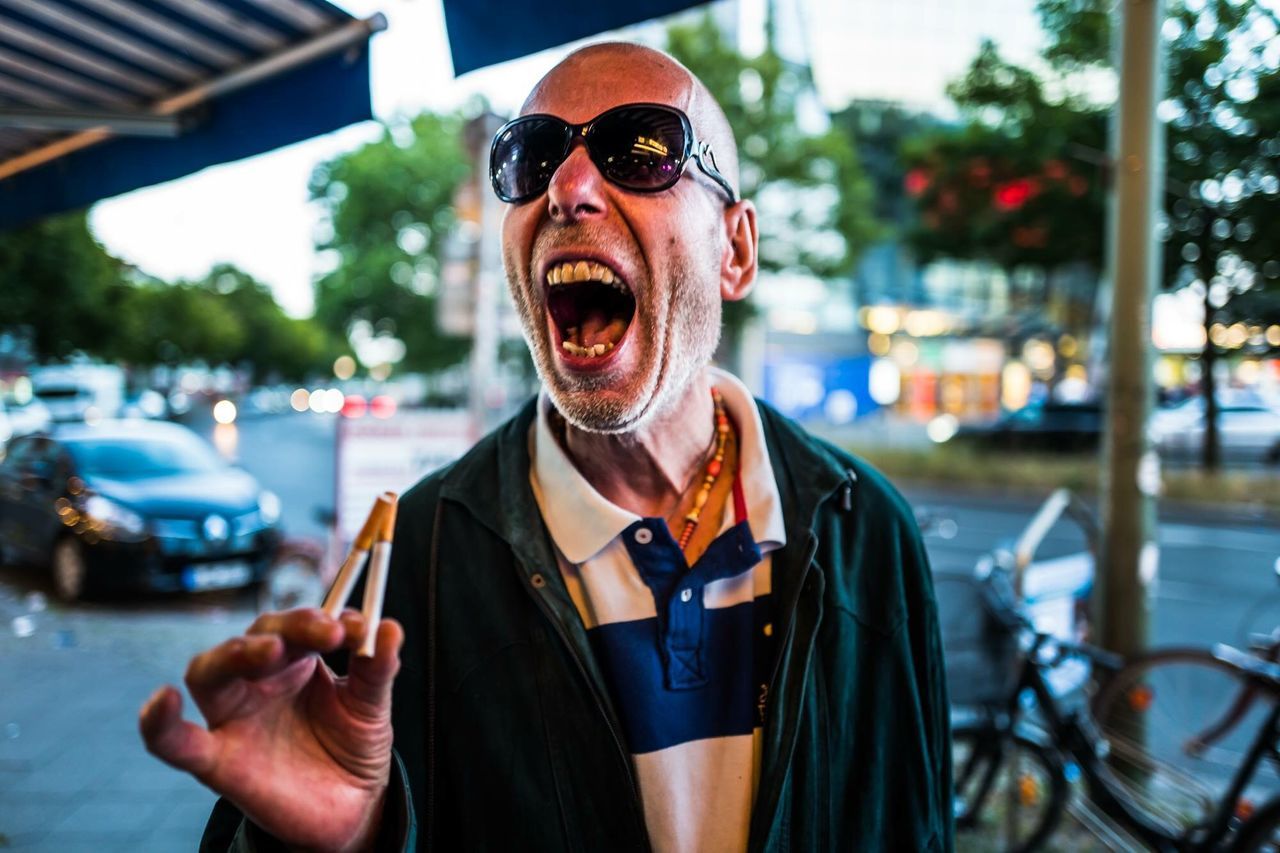 one person, glasses, sunglasses, mouth, transportation, portrait, mouth open, city, focus on foreground, mode of transportation, fashion, motor vehicle, emotion, real people, car, young adult, front view, gesturing, lifestyles, outdoors, aggression