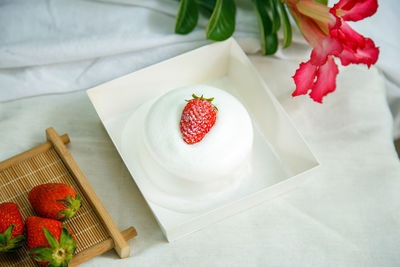 A cup of cake with strawberry fruit on top in a paper box on a white table