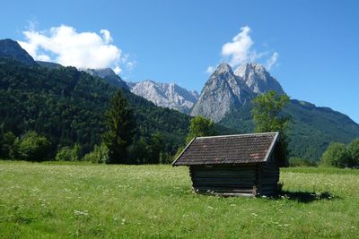 Log cabin on grassy field by mountains against sky