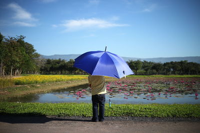 Boy with umbrella standing  by lake against sky