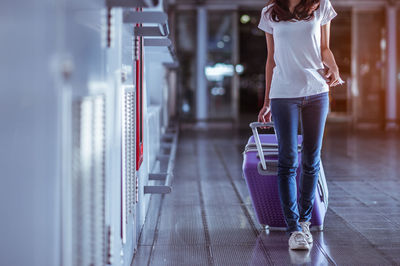 Low section of woman holding luggage and documents while walking on tiled floor at airport