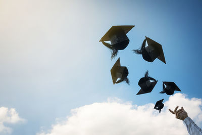 Cropped image of person throwing graduation caps against sky