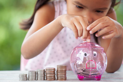 Girl putting coin in piggy bank at table