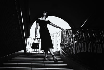 A pretty charming middle-aged woman in a black dress and sunglasses strolls through in the stairs