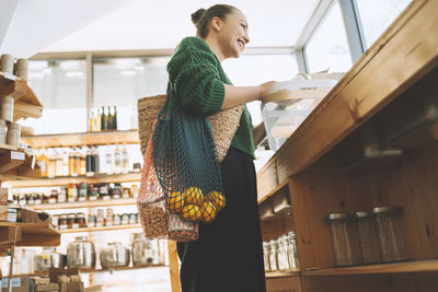 Smiling woman with fruits and groceries in mesh bags at store