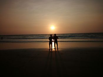 Silhouette men standing on beach against sky during sunset