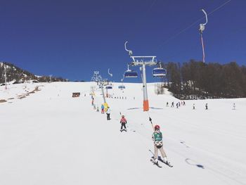 People skiing on snow covered field against clear blue sky