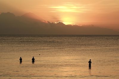 Silhouette people in sea against sky during sunset