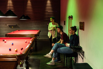 Multi-ethnic friends looking at cue balls on illuminated red pool table