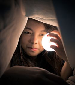 Young woman holding light bulb under duvet