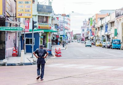 Rear view of man with hands on hips walking on street